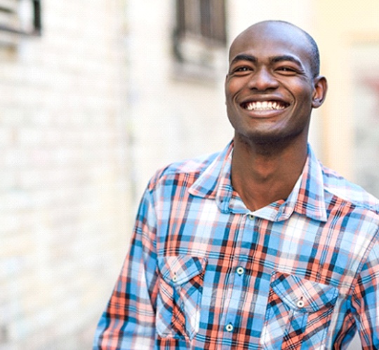 A young man wearing a plaid shirt and smiling while outside