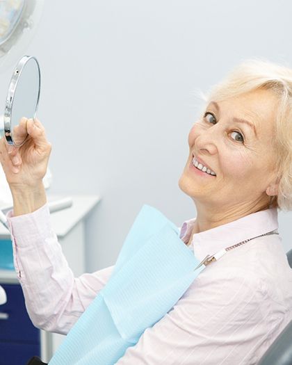 An older woman holding up a mirror at the dentist’s office after having her dental implants in Westport put into place