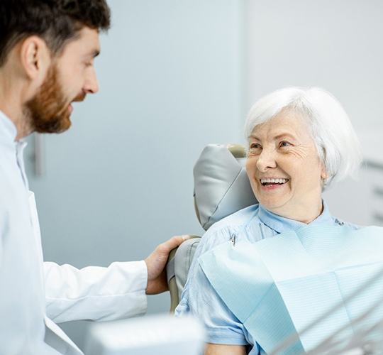 An older woman smiling at her dentist during an examination after receiving her dental implants