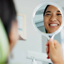 Woman smiling at reflection in handheld mirror