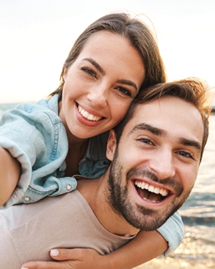 A happy couple smiling while on the beach after undergoing accelerated orthodontics in Westport