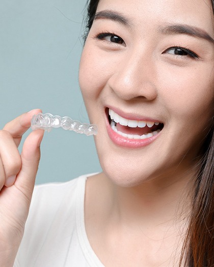 A young woman holds an Invisalign aligner in her hand that is designed to fix her overbite in Westport