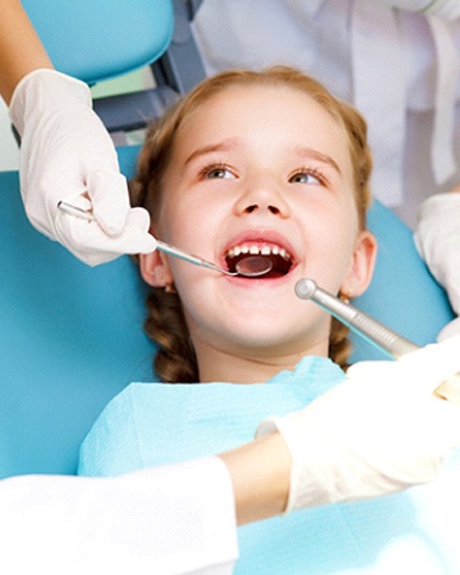 A young girl with braided pigtails smiles as her dentist in Westport examines and cleans her teeth