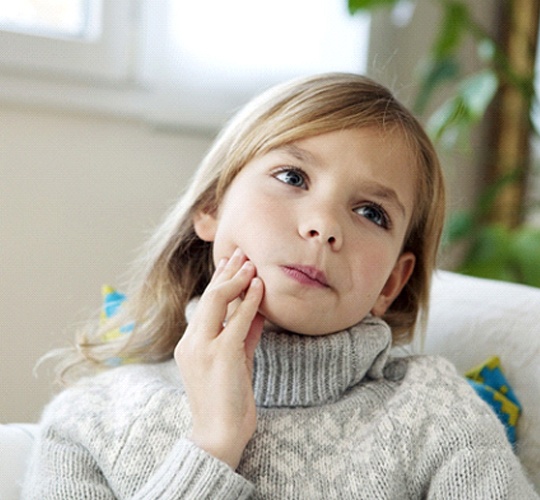 A little girl wearing a heavy sweater holds her jaw in pain because of a toothache