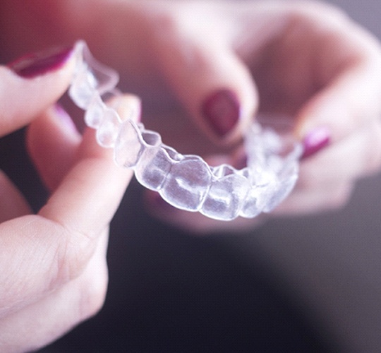 A person holding a clear Invisalign aligner between their two hands