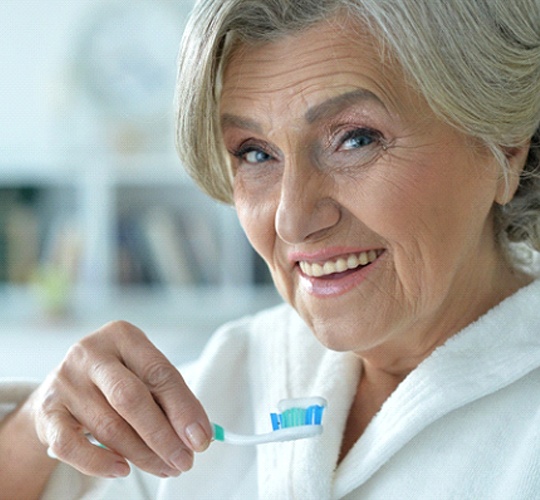 An older woman wearing a white bathrobe and preparing to brush her teeth