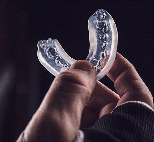 A person holding a custom-made, clear mouthguard to protect their smile