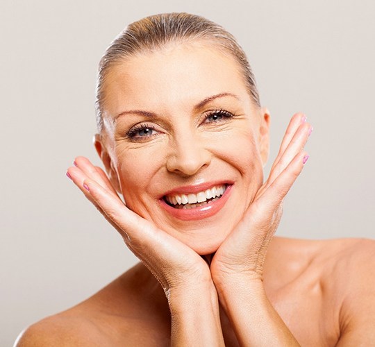 An older woman with her head between her hands and smiling after having dental implants put into place to restore her smile