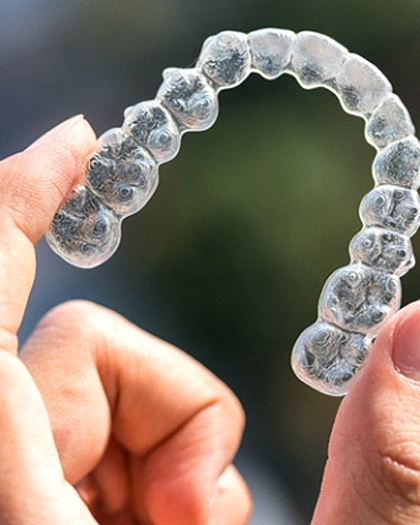 An up-close look at a person holding a clear Invisalign aligner to address crowded teeth in Westport