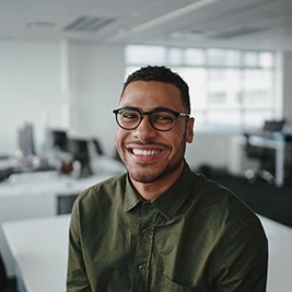 a smiling man sitting on an office desk