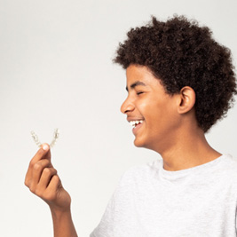 Teenage boy smiling while holding clear aligner
