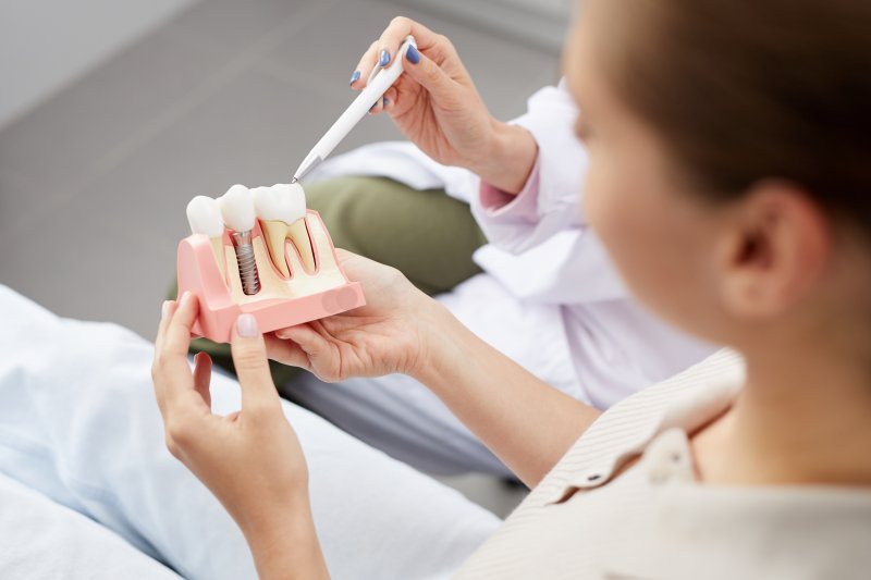 a dentist showing a female patient a cross-section of the lower arch that contains a dental implant