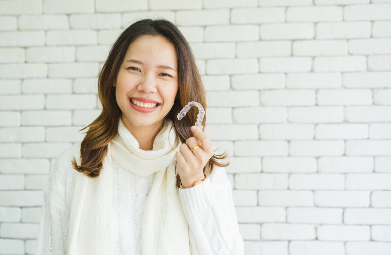 woman holding Invisalign aligner and smiling