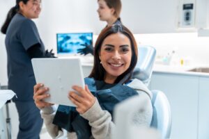 a smiling woman sitting in a dental chair holding a mirror